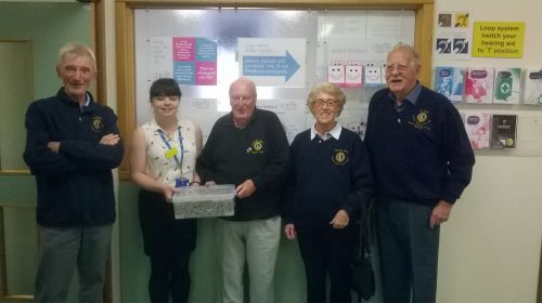 Lion Dave Lyon being presented with 900 hearing aids by a hearing dept member,accompanied by Lion Reg,,Lion Marjorie and Lion Cliflif
